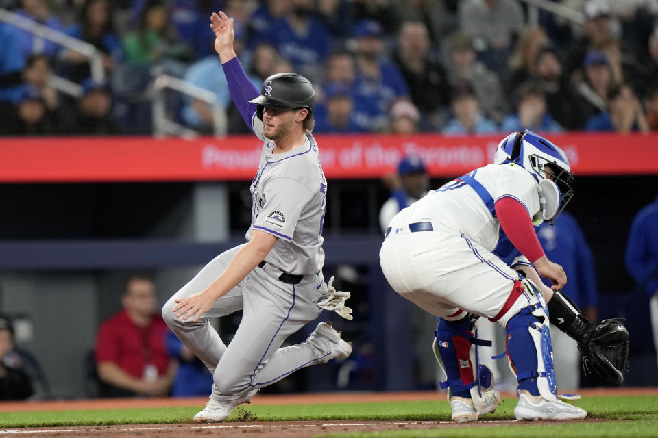 Colorado Rockies' Ryan McMahon, left, slides to score past Toronto Blue Jays catcher Alejandro Kirk, right, during third-inning baseball game action in Toronto, Friday, April 12, 2024. (Frank Gunn/The Canadian Press via AP)