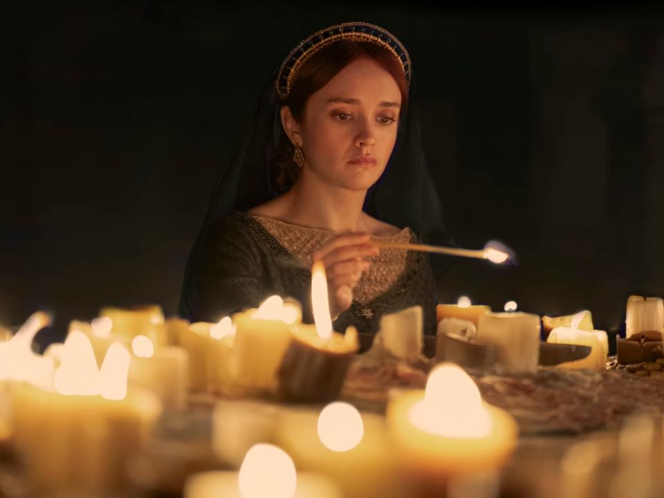olivia cooke as alicent hightower, lighting candles while wearing a green dress.