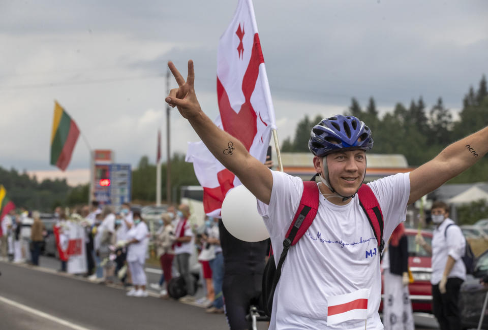 Belarusian opposition supporter rides bicycle carrying old Belarusian national flags, show victory as people create a human chain of about 50,000 strong from Vilnius to the Belarusian border during a protest near Medininkai, Lithuanian-Belarusian border crossing east of Vilnius, Lithuania, Sunday, Aug. 23, 2020. In Aug. 23, 1989, around 2 million Lithuanians, Latvians, and Estonians joined forces in a living 600 km (375 mile) long human chain Baltic Way, thus demonstrating their desire to be free. Now, Lithuania is expressing solidarity with the people of Belarus, who are fighting for freedom today. (AP Photo/Mindaugas Kulbis)