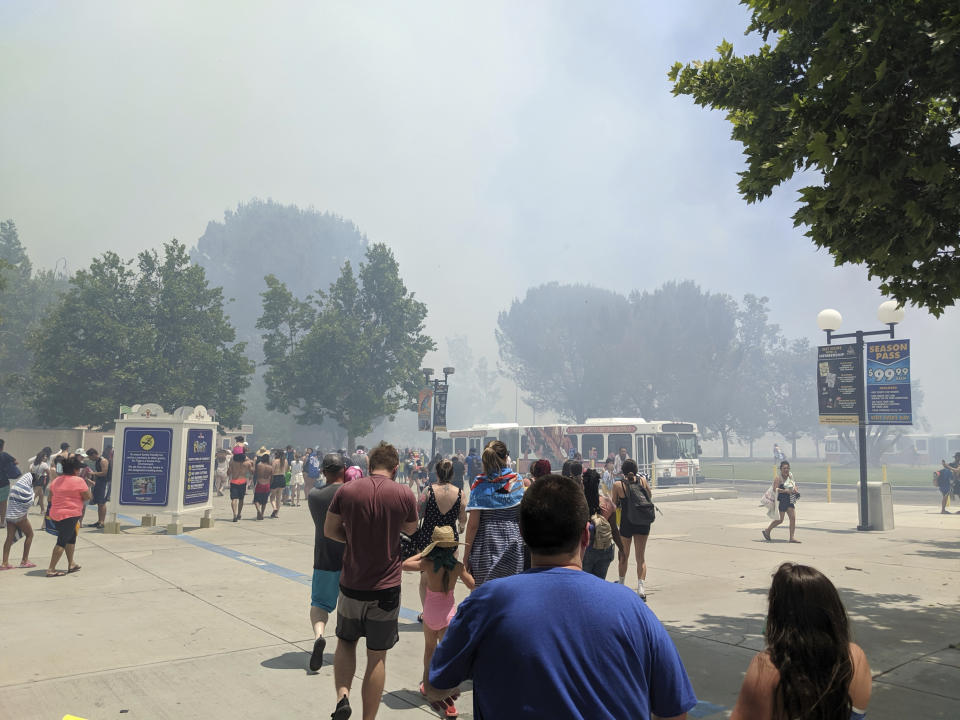 In this photo provided by Arthur Wilkie, people evacuate Six Flags Magic Mountain and Hurricane Harbor, Sunday, June 9, 2019, in Santa Clarita, Calif., north of Los Angeles, as smoke from a fast-moving brush fire surrounded the area. (Arthur Wilkie via AP)