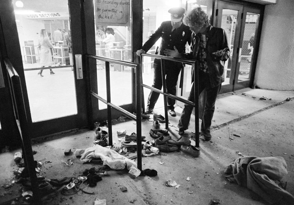 ARCHIVO – En esta fotografía de archivo del 3 de diciembre de 1979 un guardia de seguridad y un hombre no identificado revisan la zona donde varias personas murieron aplastadas durante una estampida en el riverfront coliseum de Cincinnati durante un concierto de la banda de rock británica The Who. (Foto AP/Brian Horton, archivo)