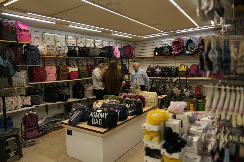 Celal Kaleli, right, talks to clients in his infant clothing and diaper bags shop in a commercial area in Istanbul, Turkey, Friday, Oct. 7, 2022. Kaleli, needs more lira to buy imported zippers and liners priced in dollars, he has to raise prices for the Turkish customers who pay him in the much-diminished local currency. “When we sell in Turkish lira, we have difficulty,’’ he said. (AP Photo/Khalil Hamra)