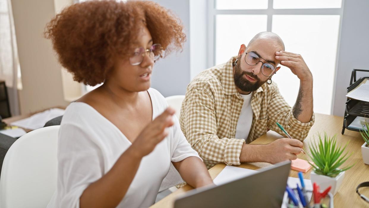 Serious man and woman coworkers stressed out, working together on laptop at office table