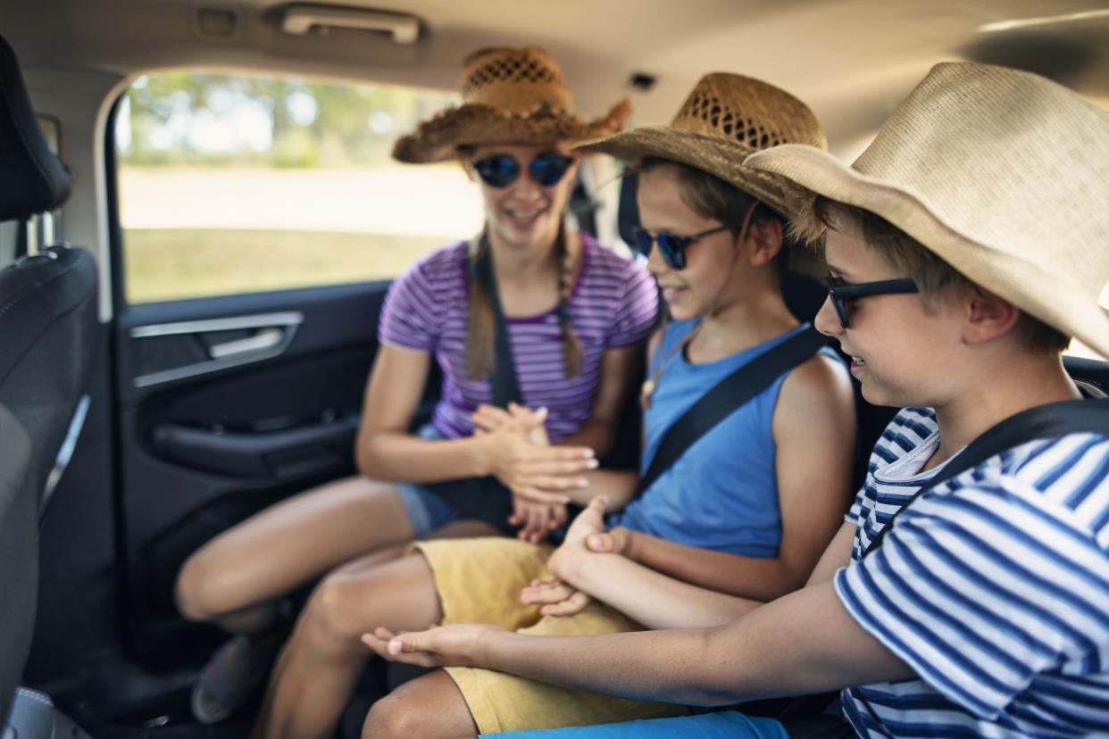 Three kids enjoying road trip in family car. Kids are aged 11 and 14. Kids wearing hats and sunglasses are playing games.Nikon D850