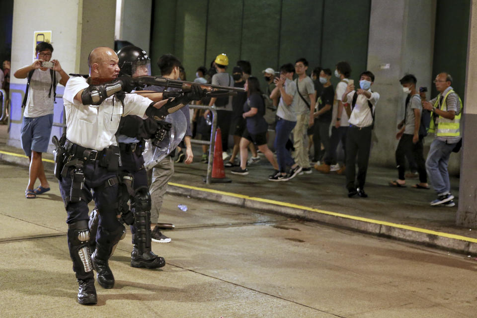 A police officer aims his shotgun at protesters during a crash near Kwai Chung police station as hundreds of protesters gather outside the police station to demand the authorities to release the protesters who have been detained with the charge of rioting during the recent protests, in Hong Kong, Tuesday, July 30, 2019. (Steve Leung/HK01 via AP)