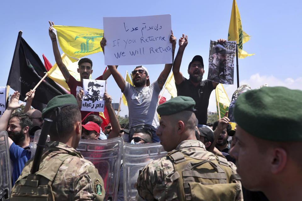 Lebanese army soldiers stand guard as Hezbollah supporters chant slogans and hold posters of the late Hezbollah military commander Imad Mughniyeh, while protesting the visit to Lebanon by Gen. Frank McKenzie, the head of U.S. Central Command, outside ​​the Rafik Hariri International Airport in Beirut, Lebanon, Wednesday, July 8, 2020. (AP Photo/Bilal Hussein)