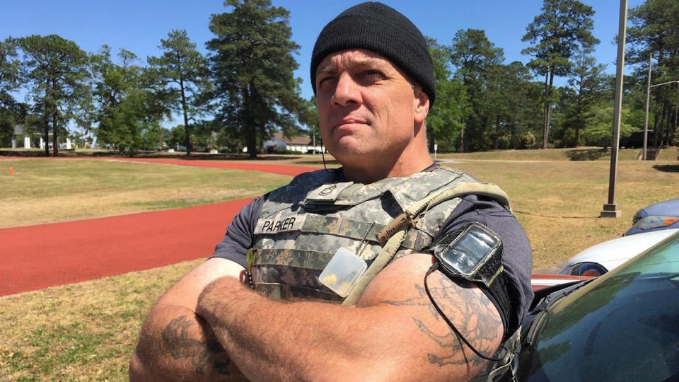 Matthew Parker leans back against a car, arms folded, next to a jogging track.