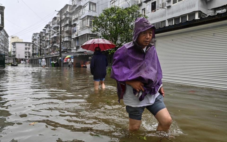 Men wade in a flooded street in a neighborhood of Ningbo, eastern China's Zhejiang province on July 25, 2021, as Typhoon In-Fa lashes the eastern coast of China - AFP 