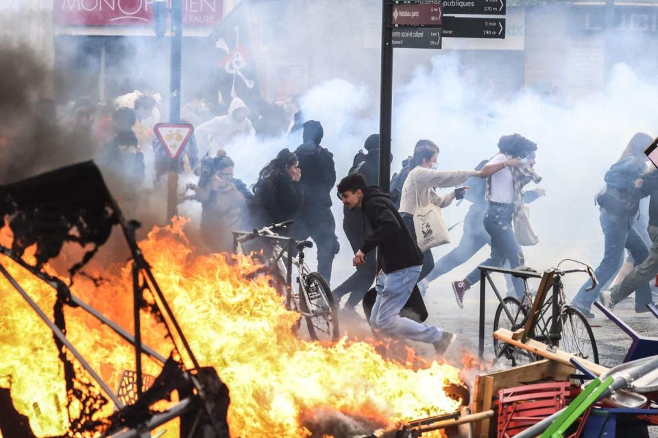 Protesters run in tear gas smoke next to   a street fire on the sidelines of a demonstration as part of a national day of strikes and protests, a week after the French government pushed a pensions reform through parliament without a vote, using the article 49.3 of the constitution, in Toulouse, southern France (AFP via Getty Images)