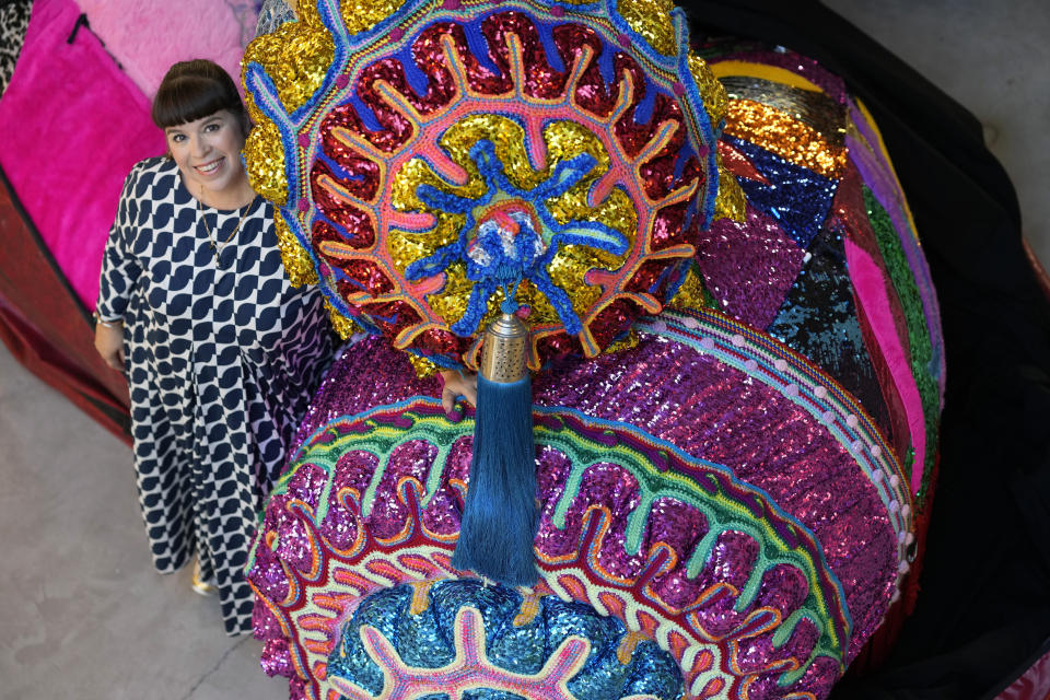 Portuguese artist Joana Vasconcelos poses for a picture by one of her works sticking out of a huge bag at her studio in Lisbon, Friday, Nov. 11, 2022. Vasconcelos has built her reputation over the past two decades. Her trademark features are large, flamboyant pieces that juxtapose the high brow and low brow, draw on Portuguese handicraft traditions, allude to women's rights, and possess a stealthy sense of humor. (AP Photo/Armando Franca)