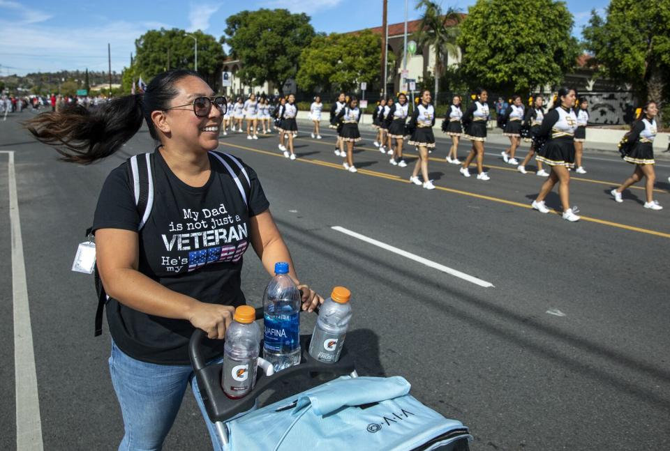A woman wheels a carriage with drinks next to a parade of cheerleaders