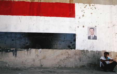 FILE PHOTO: A man sits near a poster of Syrian President Bashar al-Assad during the re-opening of the road between Homs and Hama in Talbisi, Syria June 6, 2018. REUTERS/Omar Sanadiki/File Photo