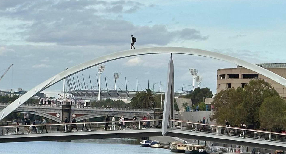 The small figure of the man can be spotted atop the Evan Walker Bridge, with people walking across the bridge on the intended footpath below.