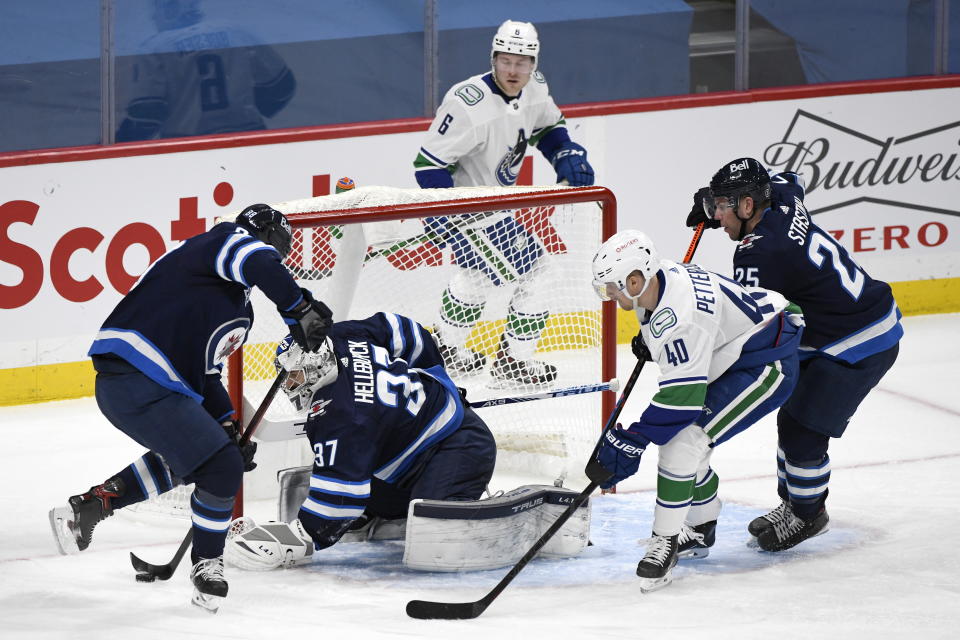 Winnipeg Jets' Nathan Beaulieu (88) clears the puck in front of goaltender Connor Hellebuyck (37) as Vancouver Canucks' Elias Pettersson (40) looks for the rebound during second period NHL hockey action in Winnipeg, Manitoba on Tuesday March 1, 2021. (Fred Greenslade/The Canadian Press via AP)