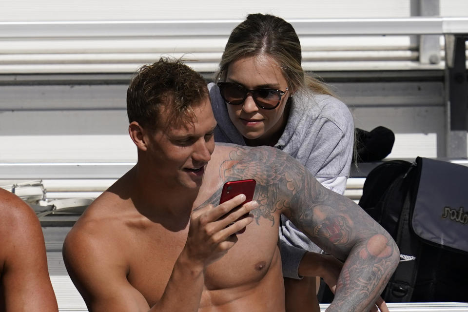 FILE - In this April 10, 2021, file photo, Caeleb Dressel, left, and his wife, Meghan Dressel, look at a phone in the stands before the TYR Pro Swim Series swim meet in Mission Viejo, Calif. For a man tabbed as swimming’s next superstar, Dressel could not be more disinterested. Of course, he cares about being fast in the pool. He just is not into anyone else’s expectations or comparisons. Fame is not his thing, either. (AP Photo/Ashley Landis, File)