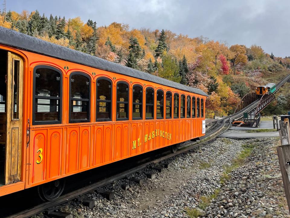 Exterior shot of an orange train on train tracks backdropped by fall trees