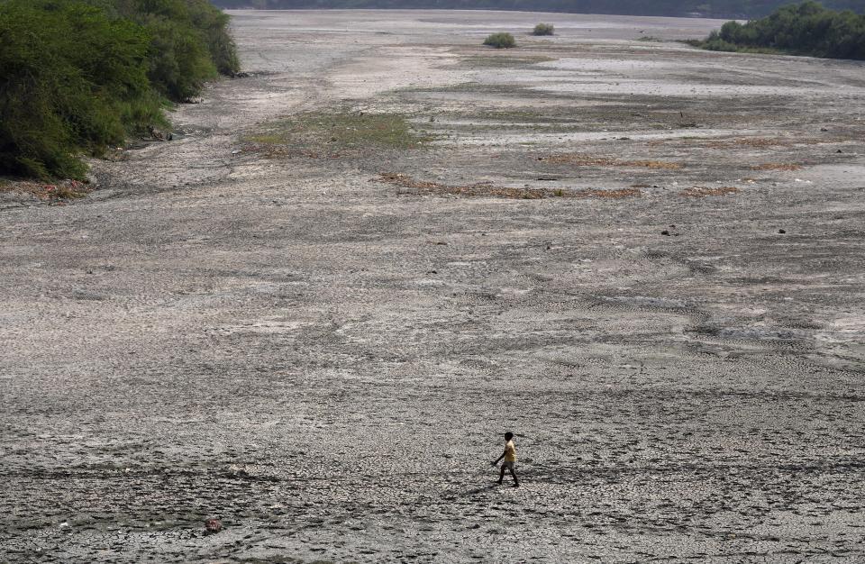 FILE - A man walks across an almost dried up bed of river Yamuna amid hot weather in New Delhi, India, May 2, 2022. In the past 30 days, nearly 5,000 heat and rainfall records have been broken or tied in the United States and more than 10,000 records set globally, according to the National Oceanic and Atmospheric Administration. Since 2000, the U.S. is setting about twice as many heat records as cold. (AP Photo/Manish Swarup, File)