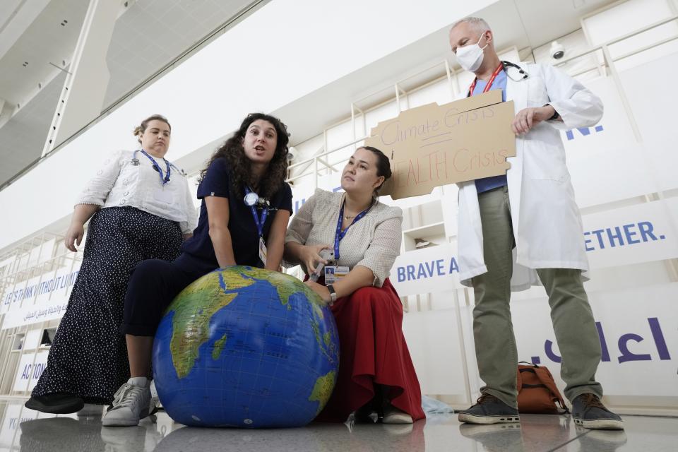 Joseph Vipond, right, Canadian Association of Physicians for the Environment, holds a sign as others pretend to resuscitate the Earth during a demonstration at the COP28 U.N. Climate Summit, Sunday, Dec. 3, 2023, in Dubai, United Arab Emirates. (AP Photo/Peter Dejong)