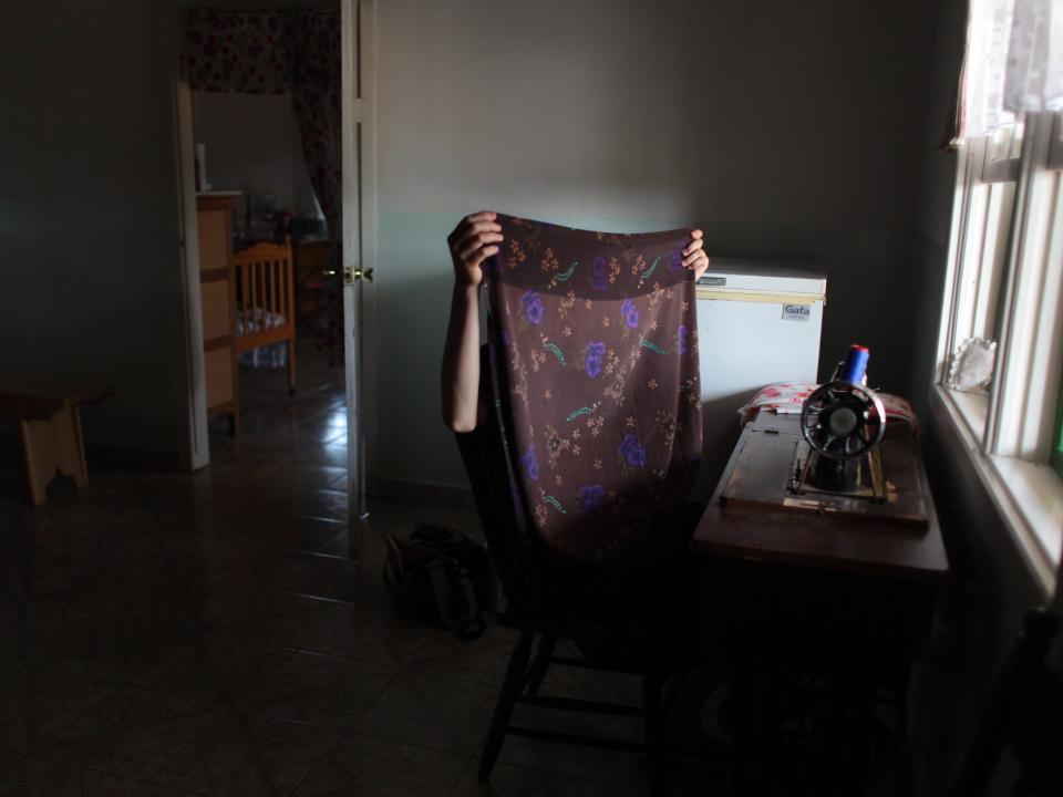 A Mennonite teenager holding colorful fabric to sew into a dress with an old fashioned sewing machine