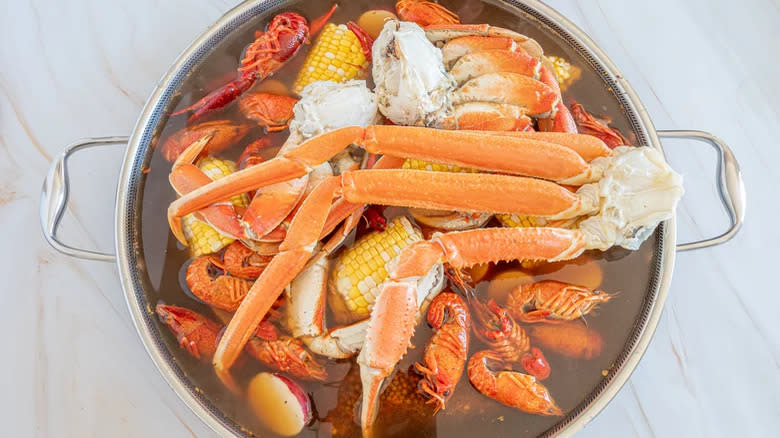 Crab legs and crayfish with corn cobs in water in pan