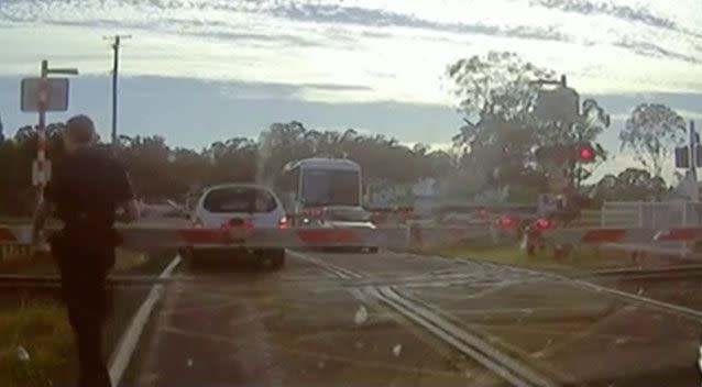 An officer can be seen walking from his car to where a Queensland motorist became stuck between two boom gates at a railway level crossing. Picture: Queensland Police