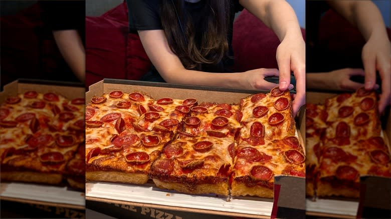 Hand grabbing deep-dish pepperoni pizza