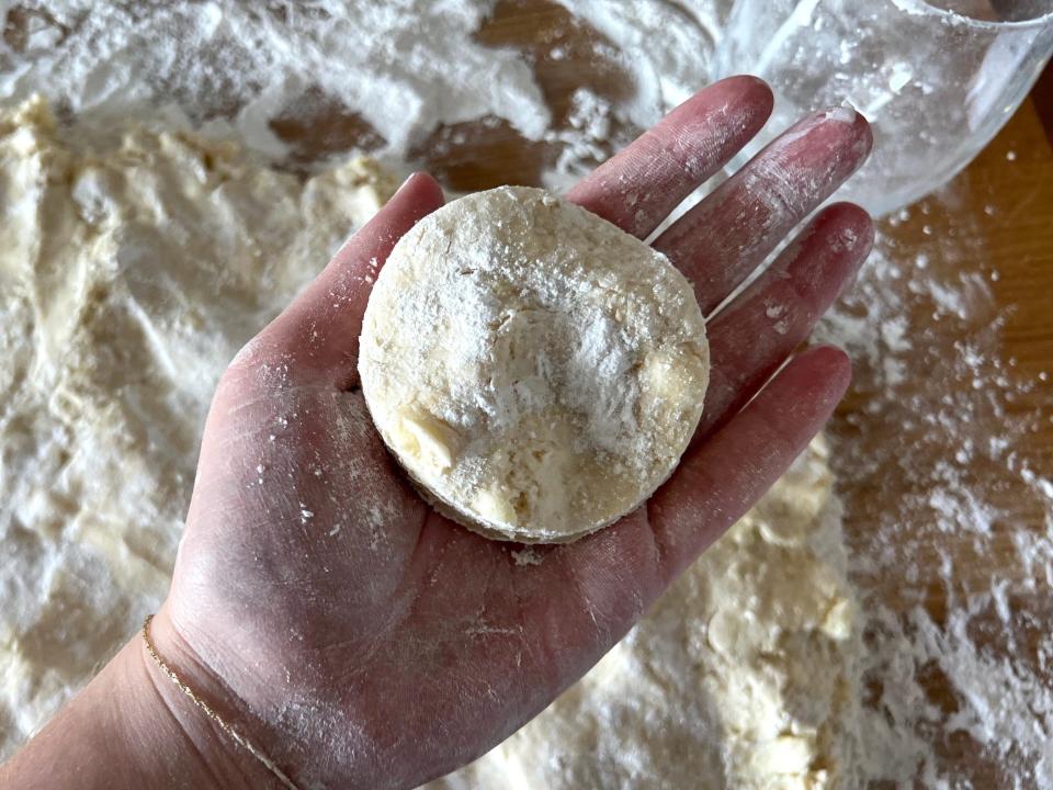 A hand holds an uncooked biscuit.