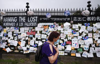 A woman passes a fence outside Brooklyn's Green-Wood Cemetery adorned with tributes to victims of COVID-19, Thursday, May 28, 2020, in New York. The memorial is part of the Naming the Lost project which attempts to humanize the victims who are often just listed as statistics. (AP Photo/Mark Lennihan)