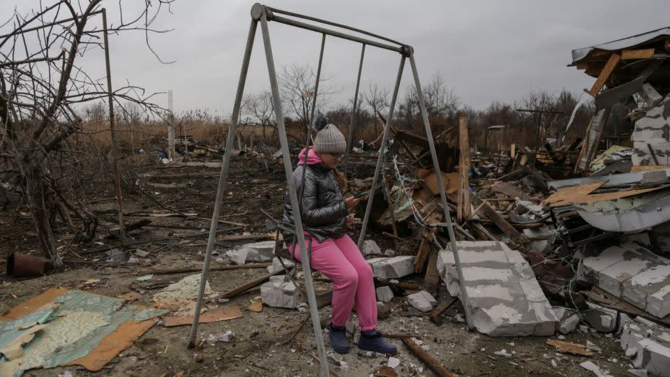 A girl uses her mobile phone while she sits on a swing at a compound of residential houses heavily damaged by a Russian drone strike in Odesa, on January 1. - Serhii Smolientsev/Reuters
