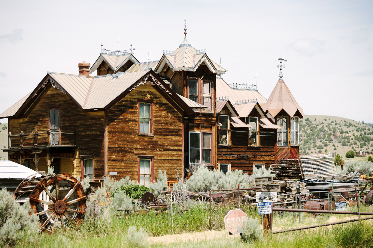 Large abandoned wooden house in the ghost town of Virginia City, Montana, yard in the foreground, hills in the background with a light blue sky