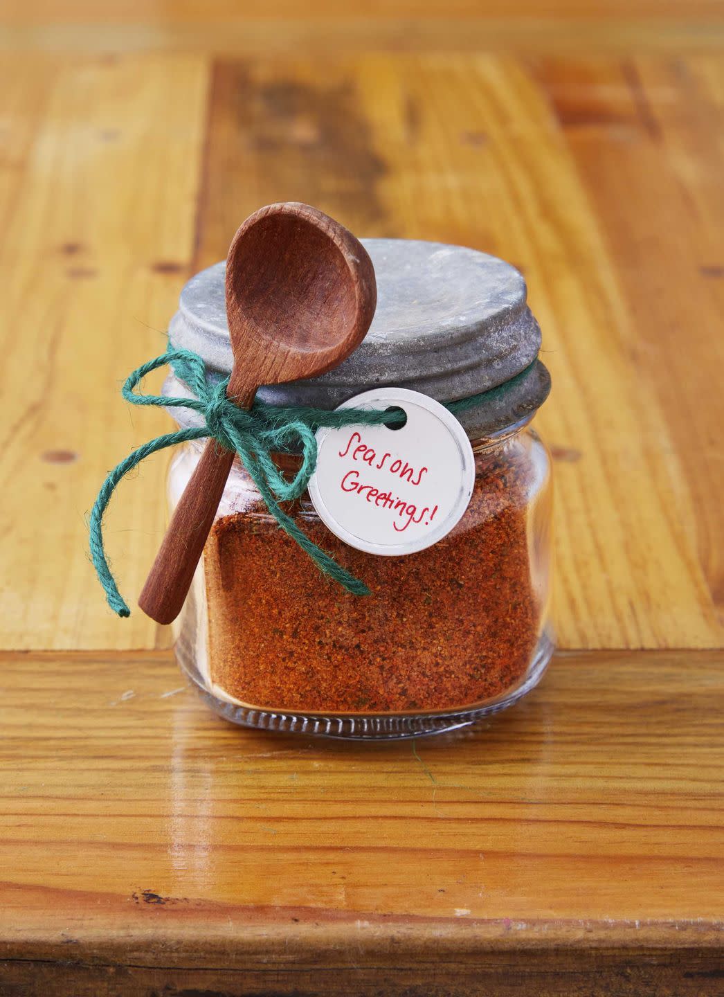 small mason jar filled with spice mix with a small wooden spoon and gift tag attached to the outside with green twinewith