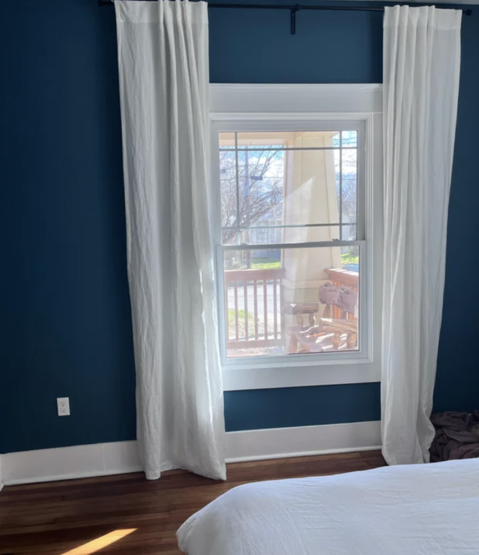 Bedroom with large window, sheer curtains, and a bed facing a wall-mounted TV