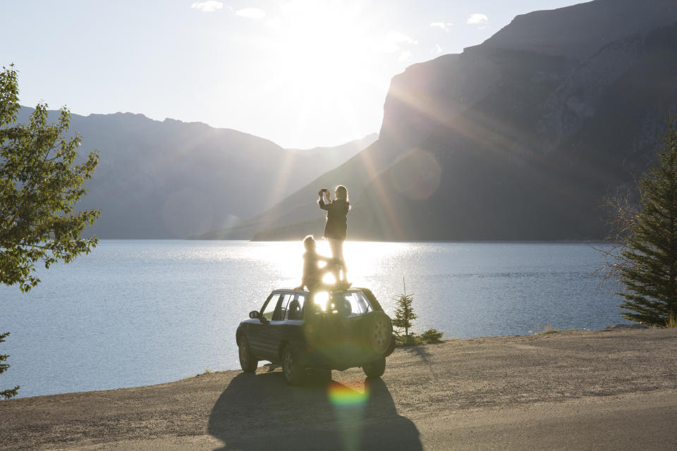 Woman takes pic from car roof while man relaxes