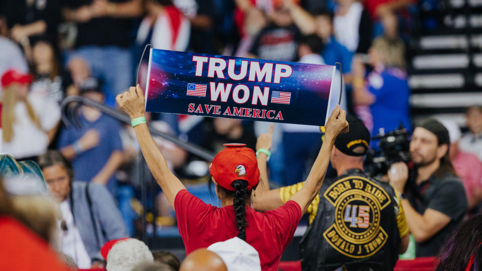 An attendee holds a banner reading: Trump Won, Save America. 