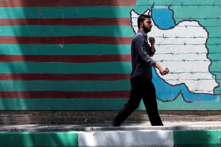 A man walks past the mural showing U.S. flag with barbed wire in Tehran