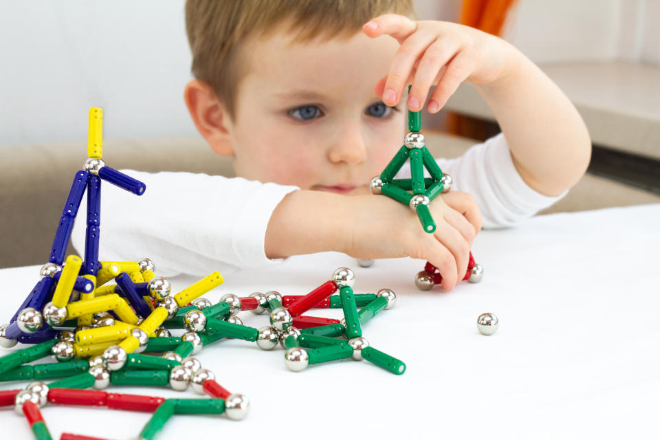 Cute child playing with lots of colorful magnet on white background