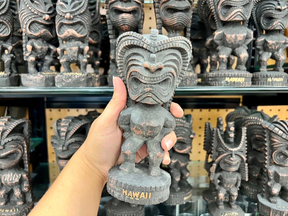 The writer holds a Tiki bobblehead in front of a shelf full of figurines