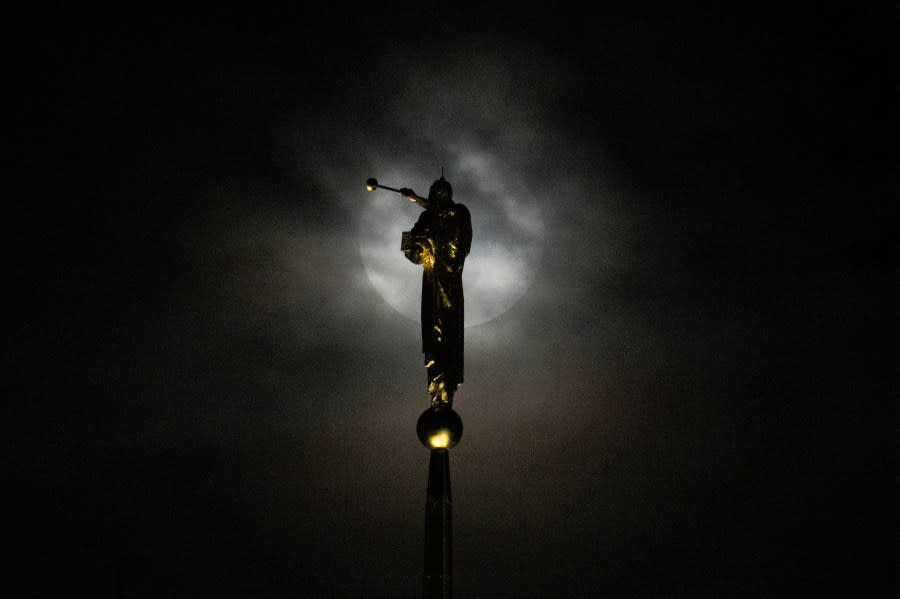 The supermoon, blue moon, rises behind a thick layer of clouds near a statue of the angel Moroni perched atop The Church of Jesus Christ of Latter-day Saints, Wednesday, Aug. 30, 2023, in Kensington, Md. The cosmic curtain rose Wednesday night with the second full moon of the month, the reason it is considered blue. It’s dubbed a supermoon because it’s closer to Earth than usual, appearing especially big and bright. (AP Photo/Julio Cortez)