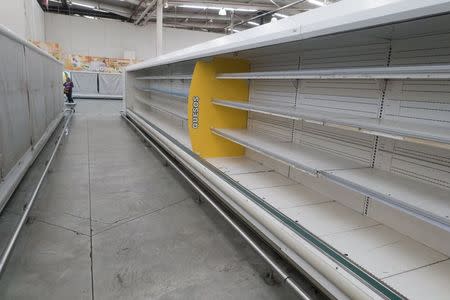 A woman is pictured past empty refrigerator shelves at a Makro supermarket in Caracas August 4, 2015. REUTERS/Carlos Garcia Rawlins