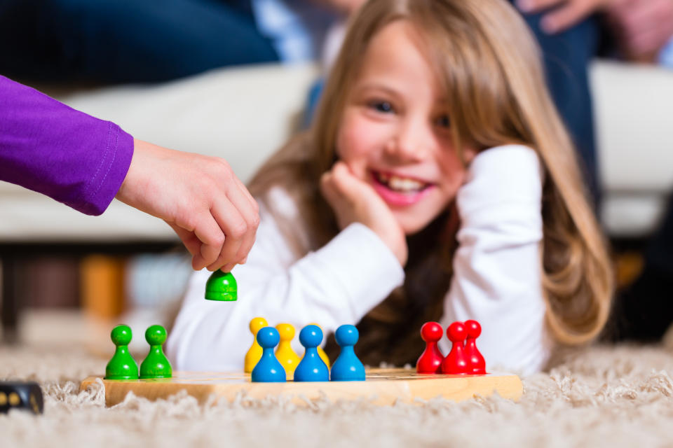 Family playing board game ludo at home on the floor, focus on the arm in front