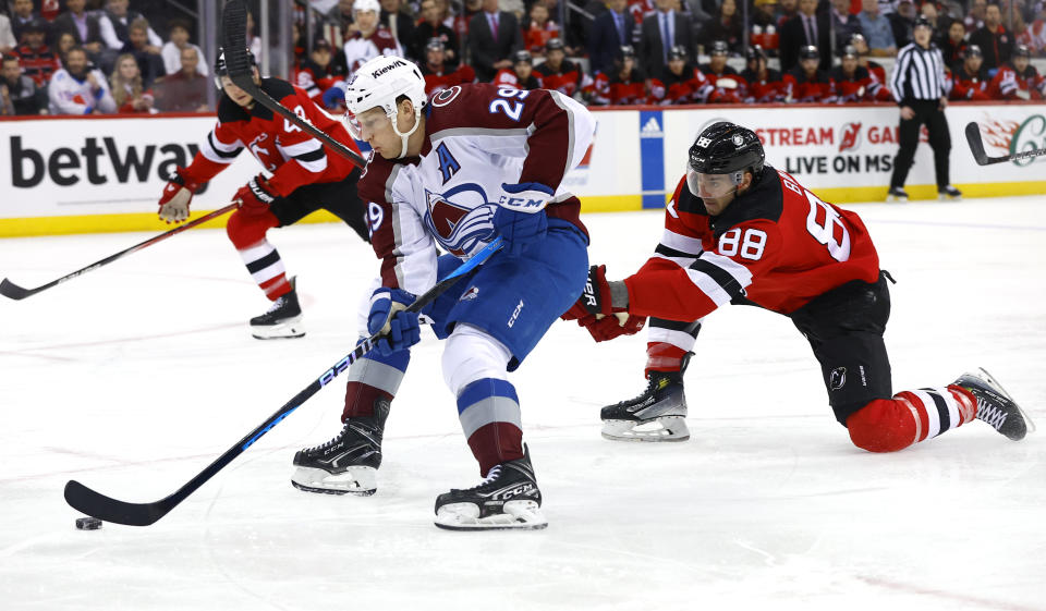 Colorado Avalanche center Nathan MacKinnon (29) skates with the puck next to New Jersey Devils defenseman Kevin Bahl (88) during the first period of an NHL hockey game Tuesday, Feb. 6, 2024, in Newark, N.J. (AP Photo/Noah K. Murray)