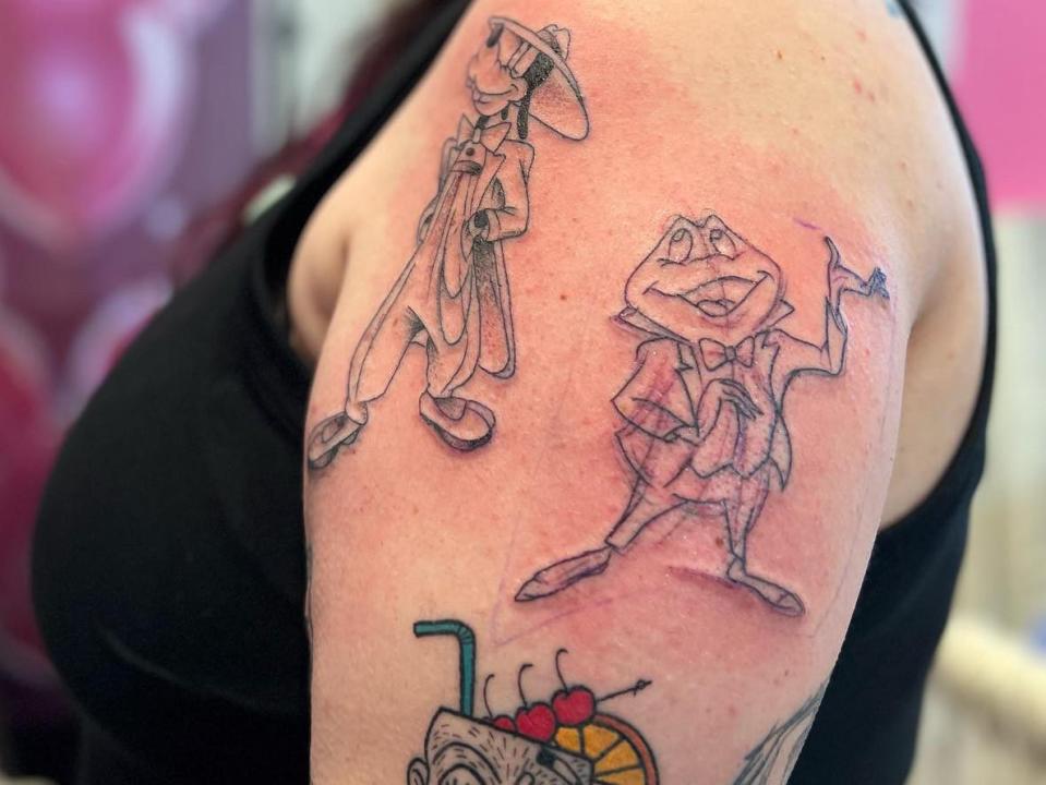 Collage of Disney characters, including a frog and Goofy on a woman's arm. Her arm is red around the tattoos