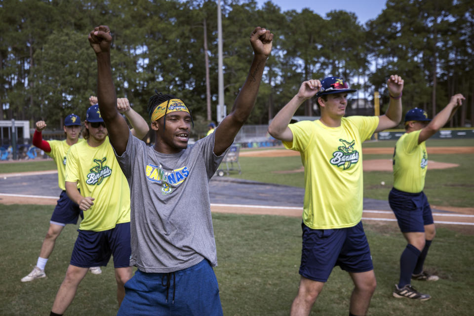 FILE - Savannah Bananas first base coach Maceo Harrison, foreground, teaches a dance routine to members of the team before a baseball game against the Florence Flamingos, June 7, 2022, in Savannah, Ga. A new exhibit dedicated to the sport's wackiest team, the Bananas, will open Friday at the Baseball Hall of Fame in Cooperstown, N.Y. (AP Photo/Stephen B. Morton, File)