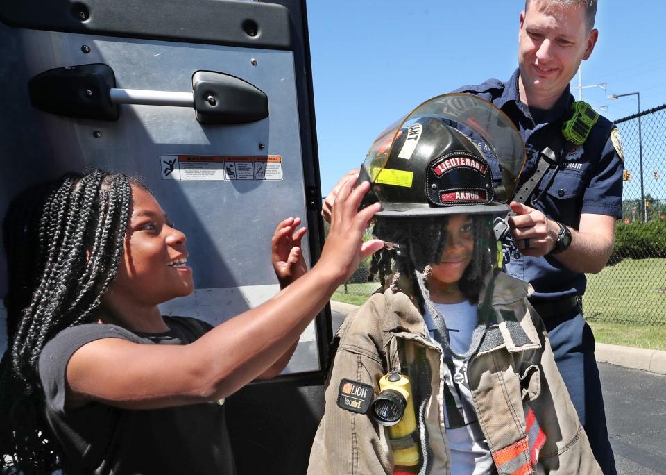 Sa'Veiyah Mays, 7, helps her brother Makahi Spragling, 9, with a helmet as Akron Fire Lt. Doug King of Fire Station 6 gets Makahi suited up in firefighter gear at the Akron Urban League event.