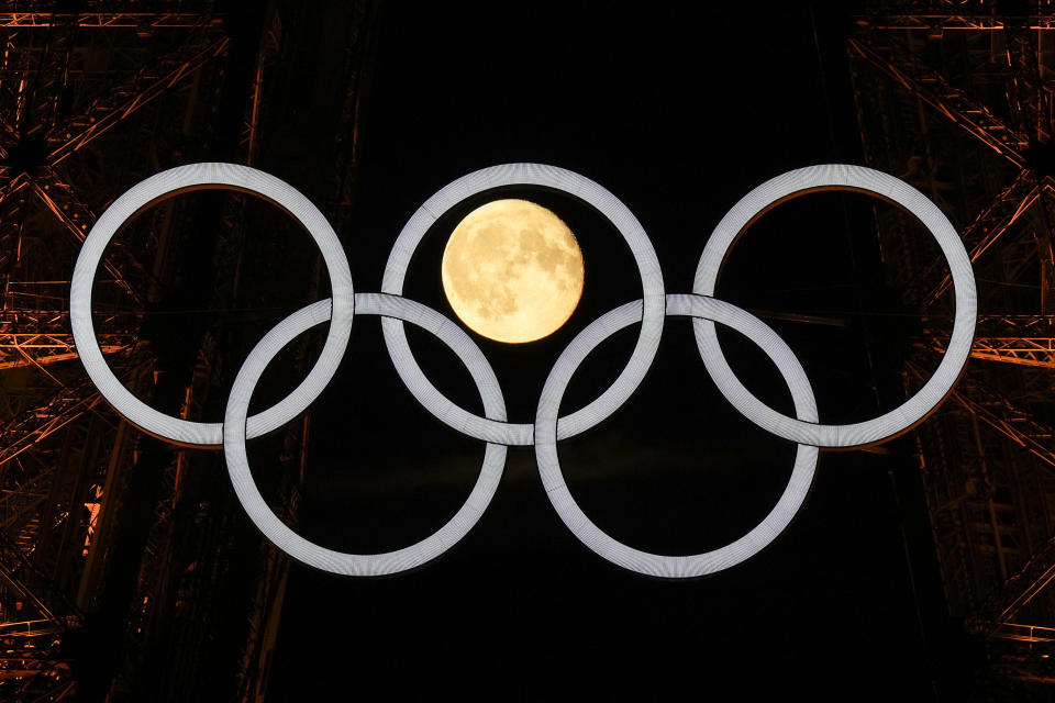 A full moon rises behind the Olympic rings hanging from the Eiffel Tower