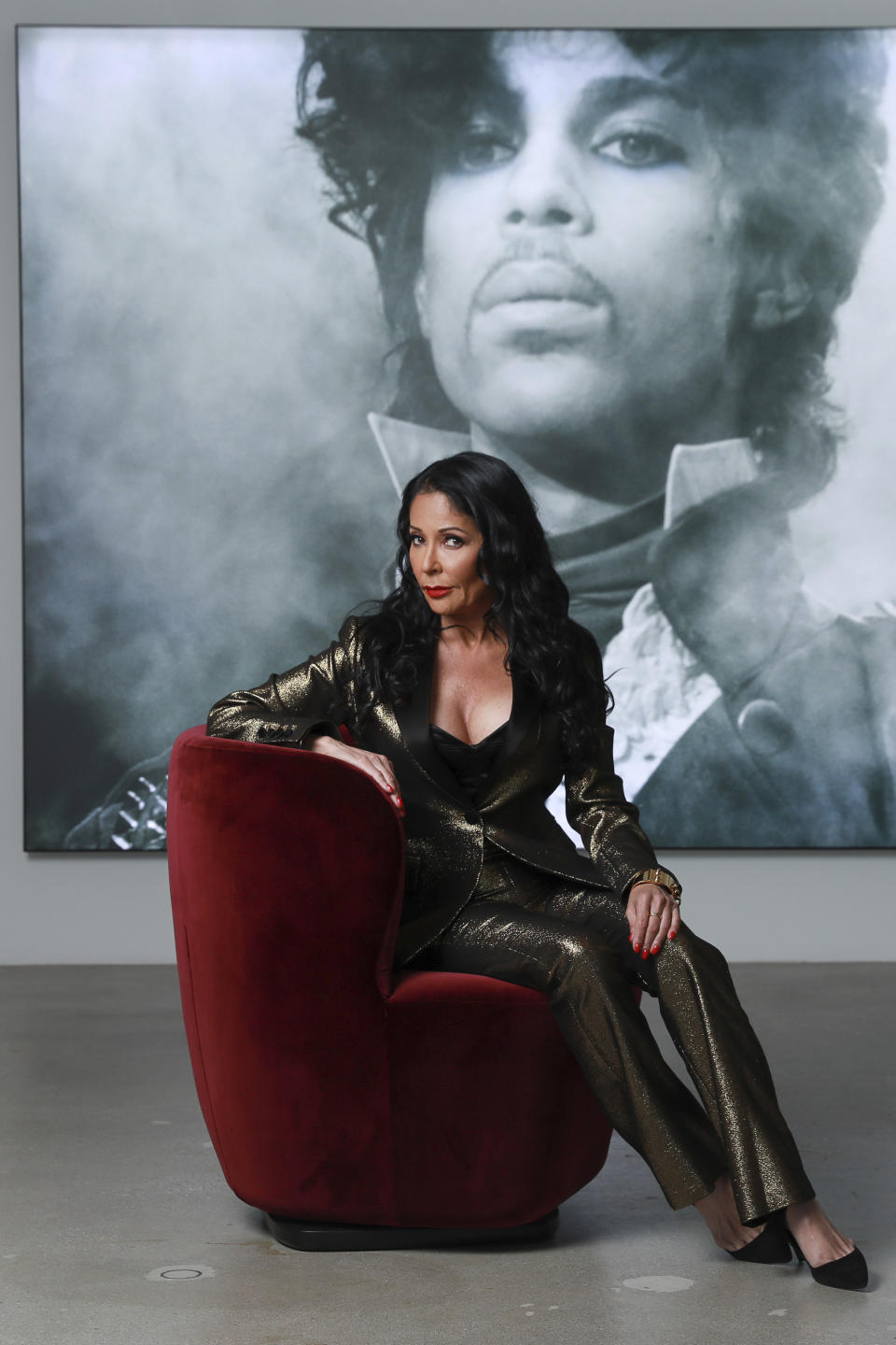 Apollonia Kotero poses for a portrait in front of a photo of Prince at Warner Music Group in Los Angeles on Friday, May 31, 2019. Kotero, who recorded Prince's "Sex Shooter," is one of several artists who spoke with The Associated Press about their experience working with the artist. The song is included on a posthumous album of Prince's music, "Originals," due out this month. (Photo by Mark Von Holden/Invision/AP)