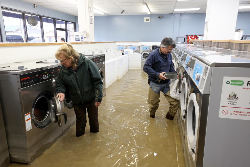 Patrick Cerruti, right, and his wife Pamela Cerruti take coins out of washing machines inside the flooded Pajaro Coin Laundry in Pajaro, California, on March 14, 2023.