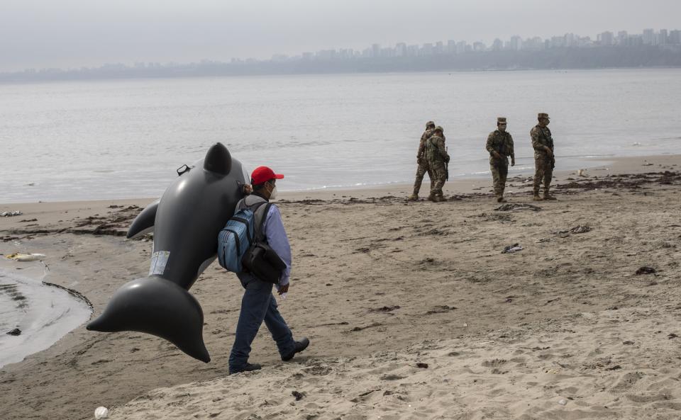 A street photographer walks as soldiers wearing masks due to COVID-19, patrol on Agua Dulce beach, in Chorrillos neighborhood of Lima, Peru, Saturday, Sept. 19 2020. (AP Photo/Rodrigo Abd)