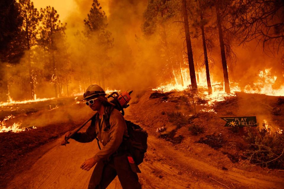 A firefighter carries a chain saw in front of a wall of flames in Sequoia National Forest.