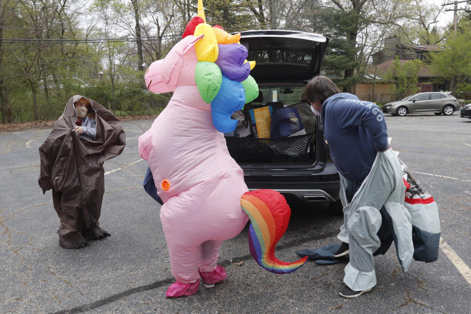 In this Monday, May 11, 2020 photo, members of the T-Rex Walking Club prepare for their walk through a neighborhood in Ferndale, Mich. The group takes its unannounced strolls through neighborhoods on a quest to bring smiles to the faces of kids, and a few adults, while under Michigan's stay-at-home order because of the COVID-19 pandemic. (AP Photo/Carlos Osorio)